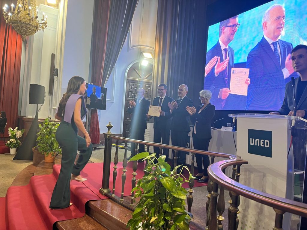 Una egresada de la UNED Valencia sube al escenario a recoger su diploma ante la mesa presidencial, donde se encuentra Javier Oliver de la AVAP, durante la ceremonia de apertura.