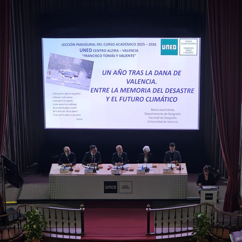Pantalla principal con el título de la lección inaugural 'Un año tras la DANA de Valencia', de M.ª José Estrela, y la mesa presidencial del acto de apertura de la UNED.