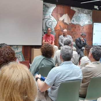 Vista general de la mesa redonda durante la jornada sobre acreditación institucional en la UPV, con los ponentes hablando frente al público en el Aula Espai-Natura.