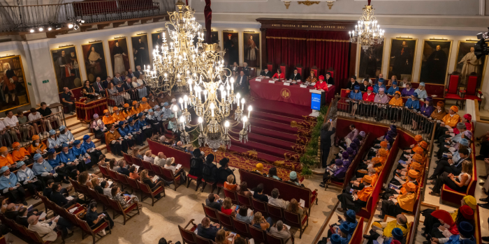 Vista panorámica del Paraninfo de La Nau durante el Solemne Acto de Apertura del Curso Académico de la Universitat de València, con autoridades en la mesa presidencial y académicos vestidos con birretes y togas de colores en los asientos.