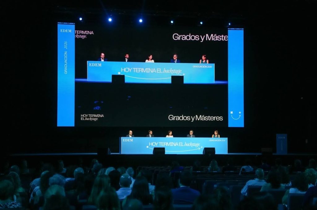Vista del escenario durante el acto de graduación de grados y másteres de EDEM Escuela de Empresarios en el Roig Arena de València, con la mesa presidencial y una gran pantalla con el lema «Hoy termina el backstage».